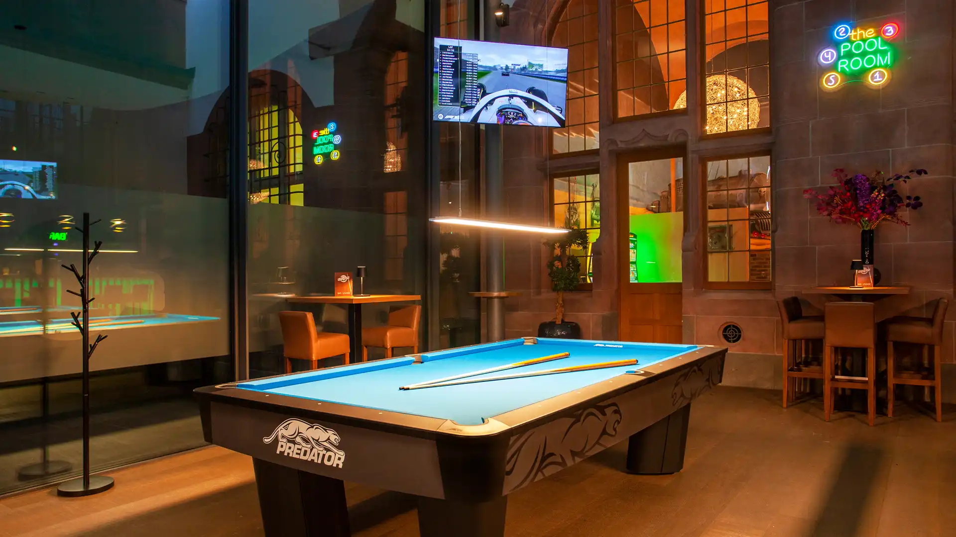 Predator-Tisch vor den historischen Bogenfenstern mit Neon-Schriftzug „the Pool Room“.
