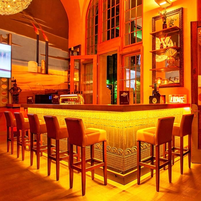 Die beleuchtete Bar der Pool-Station mit Ledermöbeln und historischen Bogenfenstern